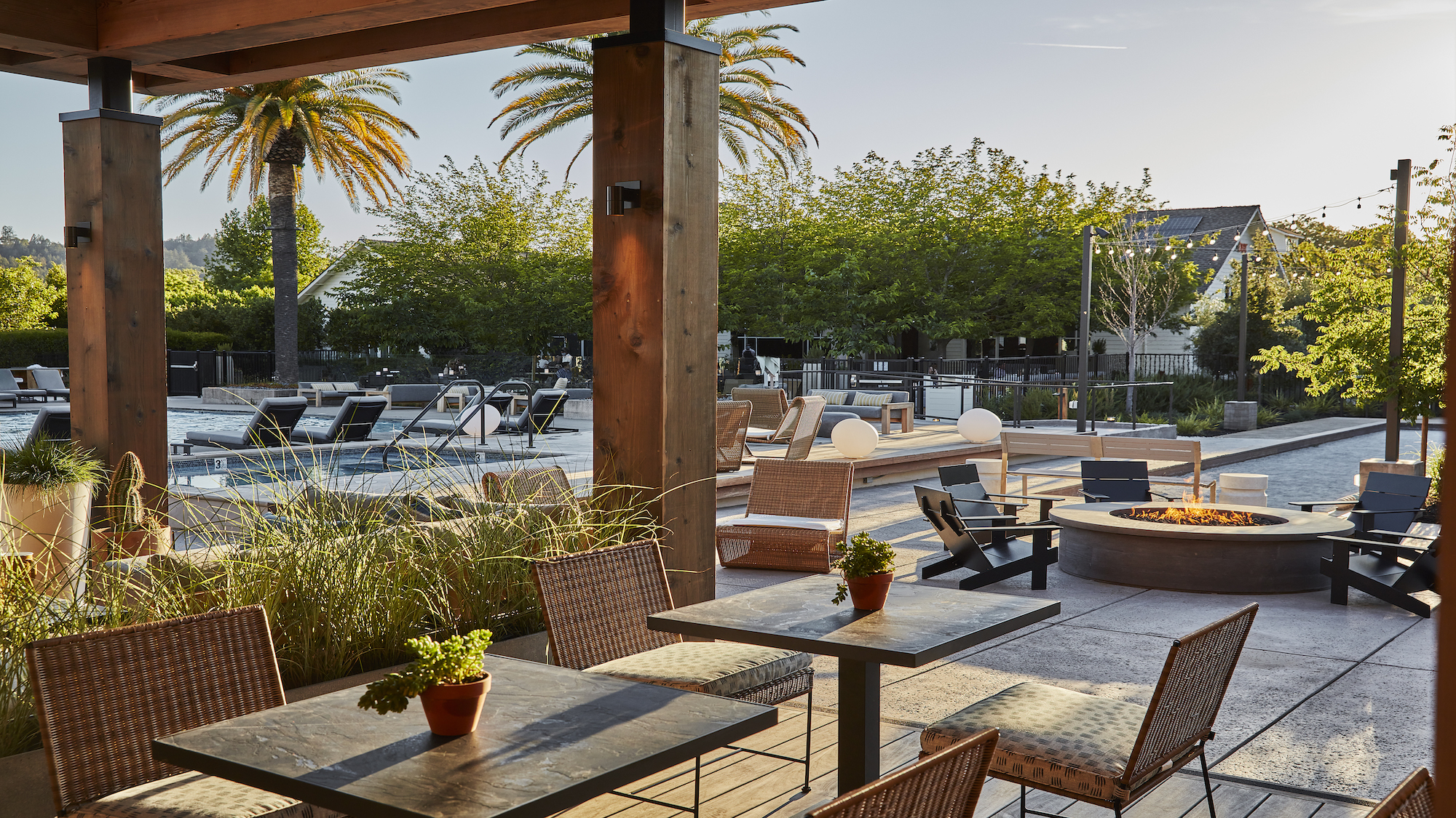 Deck of a pool with tables of a restaurant, pirepit, and lounge chairs at one of the best wellness retreats in the US